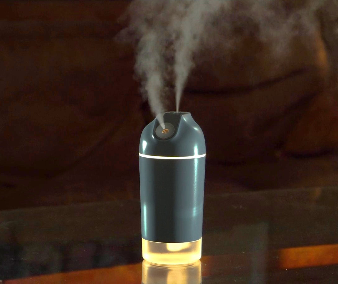 A small tabletop humidifier emitting a fine mist, shown on a reflective surface with a softly blurred indoor background.