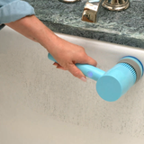 A person using a light blue handheld electric bathtub scrubber on the inside of a white bathtub, with a dark marble countertop and chrome faucet visible in the background.