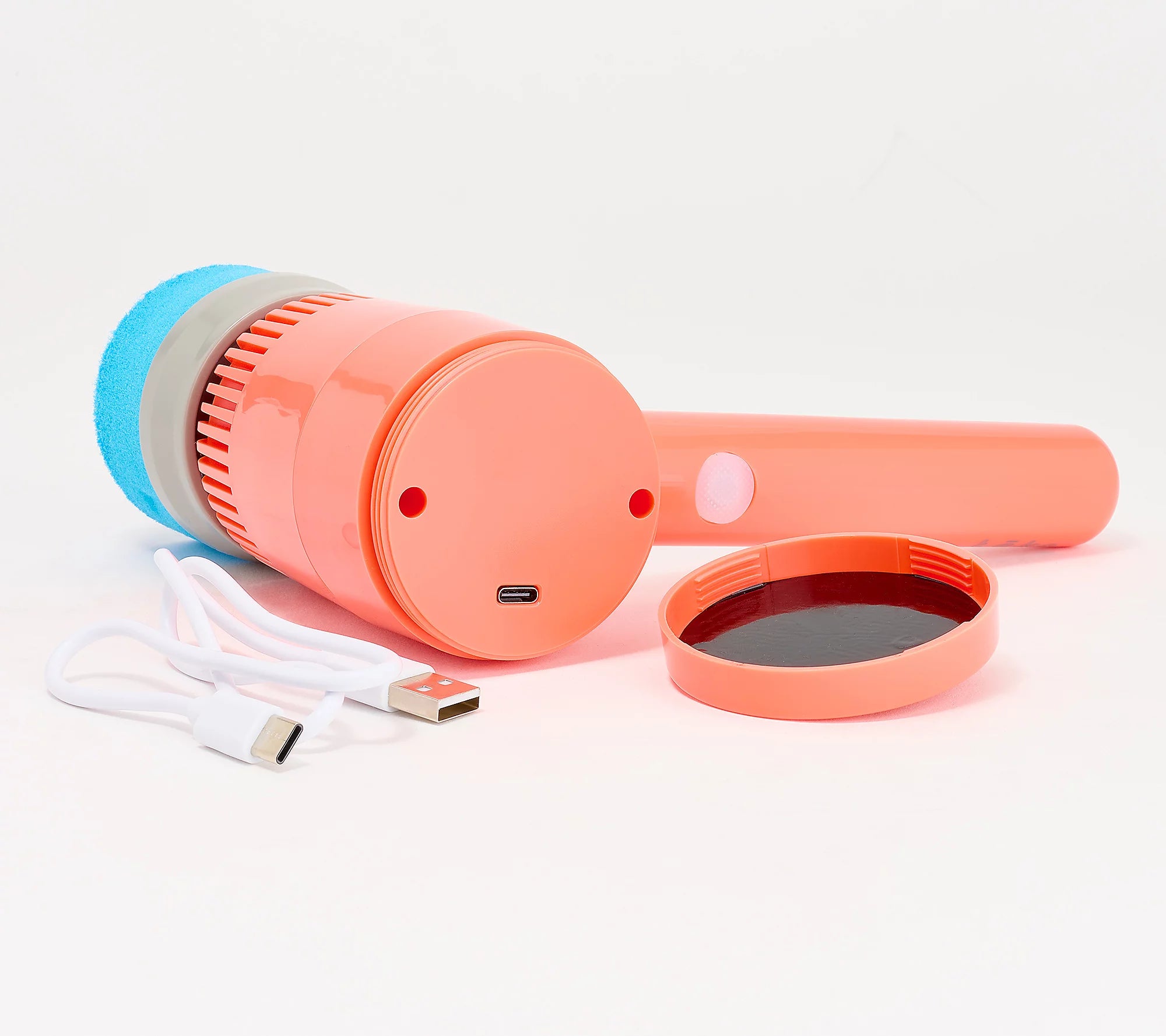 An orange handheld electric cleaning brush with a blue foam head, shown with its white USB-C charging cable and a separate orange lid on a white background.